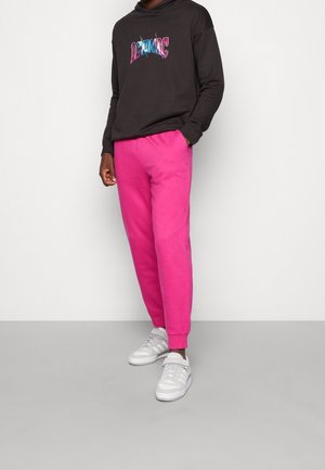 Haut à capuche noir avec un graphique "ICONIC" en bleu et rose. Pantalon de survêtement rose avec des poignets élastiques. Baskets blanches avec des accents gris.