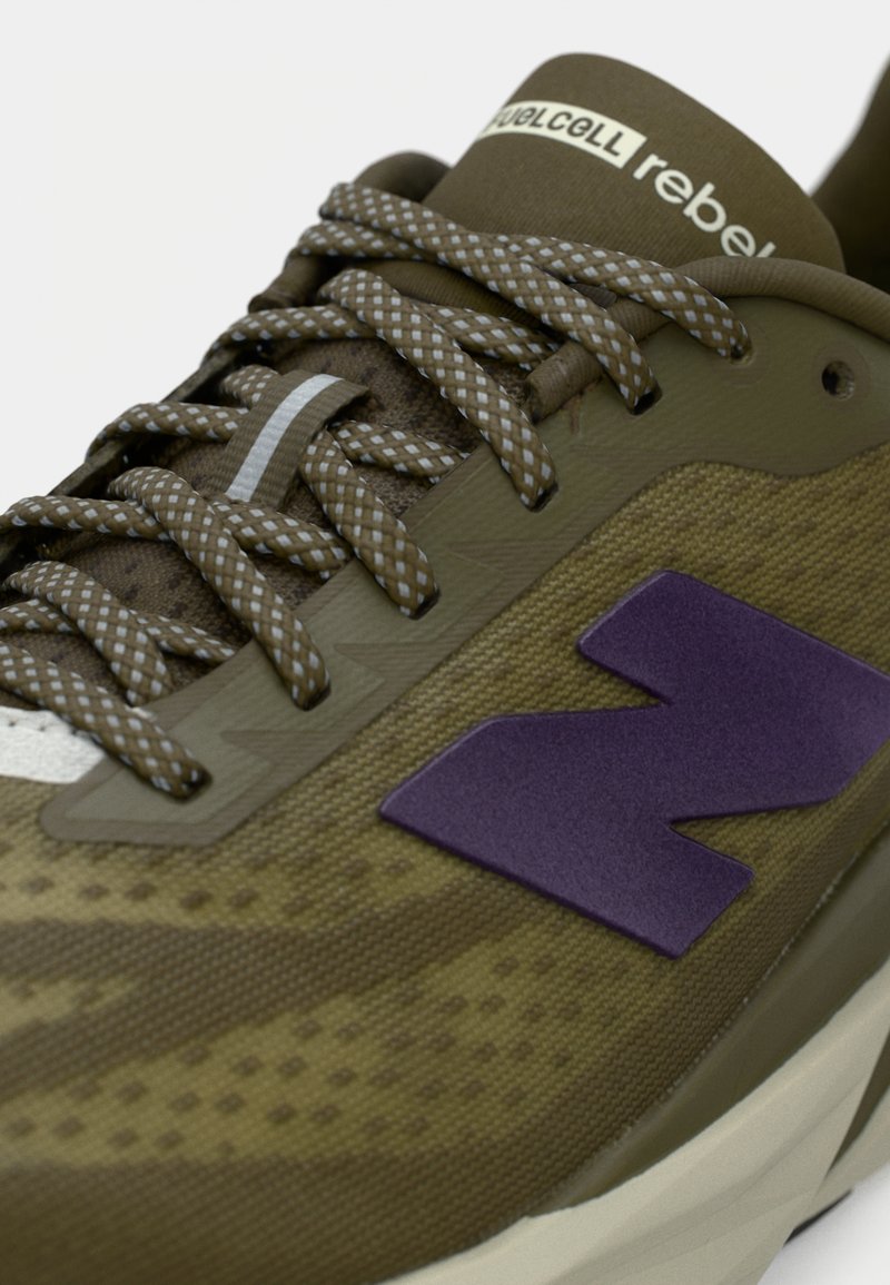 Olivengrøn løbesko med en tekstureret mesh-overdel, lilla logo og grå snørebånd. Har en polstret sål og mønstrede detaljer.