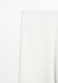 Close-up of white garment fabric with visible seam and topstitch detail on a plain white background.