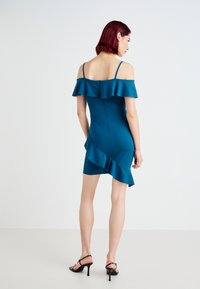 Vestido teal ombro a ombro com bainha em babados e silhueta ajustada. Apresenta alças finas e fecho nas costas. Textura de tecido suave.