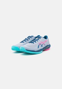 Baskets de sport gris clair avec une tige en maille, des accents bleus et un logo rose. Dotées d'une semelle turquoise avec un motif de grip texturé.
