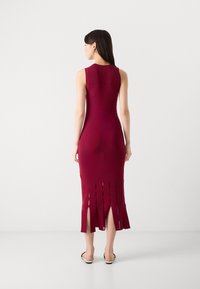 Bordowa dzianinowa sukienka bez rękawów o dopasowanym kroju i bocznymi rozcięciami na dole. Gładka tekstura i minimalistyczny design.