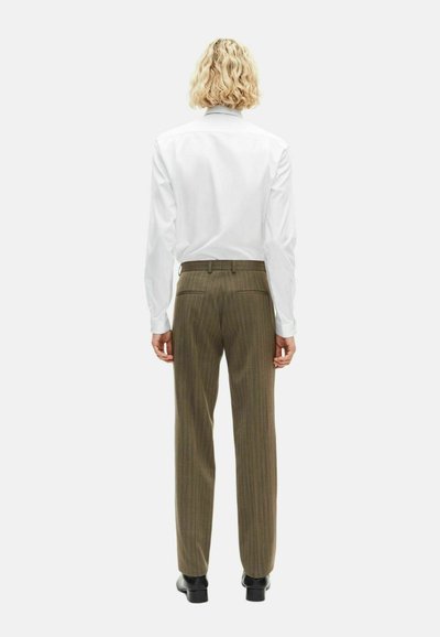 Witte lange mouw shirt en olijf groene gestreepte broek met een rechte snit. De outfit is gecombineerd met zwarte schoenen.