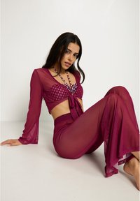 Conjunto de dos piezas de color burdeos, con un top corto atado que presenta detalles estampados y pantalones de pierna ancha, enfatizando un tejido ligero y fluido.