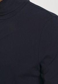 Mørkeblå rullekrave top med en glat tekstur, minimal syningsdetaljering og en tætsiddende pasform, der viser en høj halsudskæring og ensfarvet design.