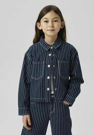 Chaqueta de mezclilla azul marino con rayas verticales blancas, dos bolsillos delanteros y botones plateados. Presenta un cuello con solapa y un corte relajado.