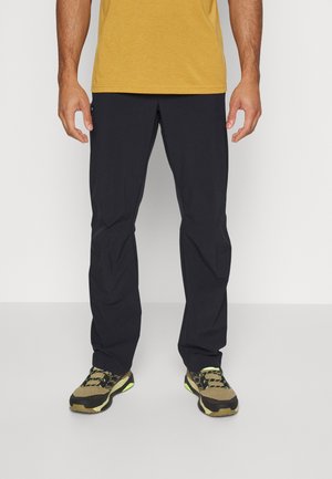 Marineblauwe lichte broek met een relaxte pasvorm, met een gladde textuur en elastische tailleband, gecombineerd met olijfkleurige en zwarte sportschoenen.