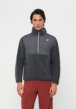 Fleece-genser i mørk grå med høy krage, halv glidelås og teksturert kropp. Har glatte ermer og logo på brystet.