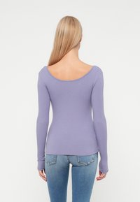 Langermet, tettsittende topp i ribbet lavendelstoff med vid halsåpning og tommelhull, kombinert med medium-vaskede blå jeans.