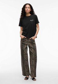 T-shirt nera in cotone con logo, abbinata a pantaloni a gamba larga con stampa leopardata in tonalità di marrone e nero. Tacchi aperti neri completano il look.