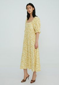 Geel zebra-print midi-jurk met puffmouwen, vierkante halslijn en geraffineerde taille. Gepaard met bruine hoge hakken sandalen.
