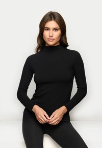 Schwarzes Rollkragenoberteil aus dehnbarem Stoff mit langen Ärmeln, tailliertem Schnitt, glatter Textur und hohem Kragen. Getragen mit schwarzen Leggings.