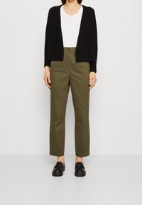 Svart kortärmad cardigan, vit åtsittande t-shirt, olivgröna rakbenade byxor och svarta klackar. Enkelt designade med rena linjer och inga mönster.