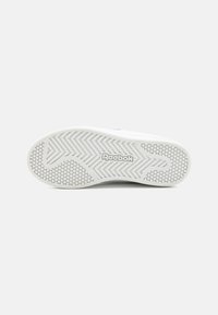 Hvit gummisåle på joggesko med fiskebein- og sekskantmønstre. "Reebok"-logo preget på siden. Glatt overflate.