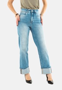 Jeans de tiro alto en un azul claro, con pierna recta y dobladillos vueltos. Tienen una textura de mezclilla suave y detalles de costura en contraste.