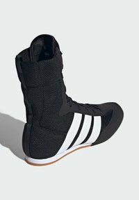 Czarne sportowe buty za kostkę z siateczkowego materiału, gumową podeszwą i trzema białymi paskami po bokach. Posiadają sznurowadła i wyściełany kołnierz.