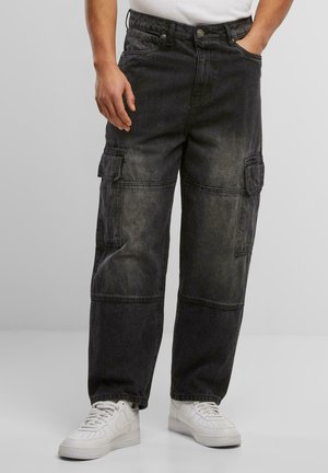 Black cargo pants with a faded texture, multiple pockets, and a loose fit. Paired with white sneakers for a casual look.