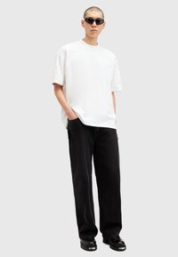 White textured t-shirt with embossed lettering, paired with loose-fitting black denim pants and glossy black ankle boots.