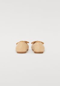 Ballerines tissées beiges avec une finition texturée semblable à de la paille et deux petits nœuds à l'avant. Bout arrondi et semelle plate en caoutchouc.