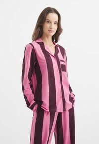 Raidallinen vaaleanpunainen ja tummanlila yöasu, joka sisältää napitettavan paidan taskulla ja vastaavat housut, valmistettu pehmeästä, hengittävästä kankaasta.