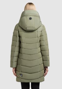 Groene gewatteerde jas met een chevronpatroon, grote capuchon en een zwart logo-oproep aan de onderkant. Glad textuur en een middellange ontwerp.