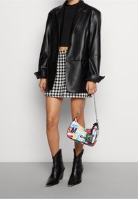 Blazer en cuir noir, top noir raccourci, jupe en pied-de-poule noire et blanche, sac imprimé coloré, bottines à talons noires.