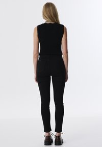Zwarte mouwloze top gecombineerd met hoge zwarte skinny jeans. Inclusief achterzakken en textuurstof. Zwarte schoenen met een dikke zool.