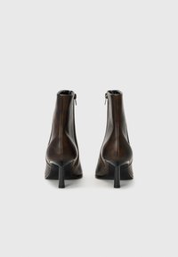 Bottines en cuir marron avec un design épuré, dotées d'une fermeture à glissière sur le côté et d'un talon fin. Texture lisse avec des détails de couture minimaux.