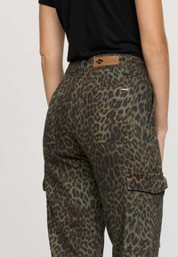 Pantalons cargo imprimés léopard avec une palette de couleurs verte et brune, plusieurs poches et un patch en cuir avec marque à la taille.