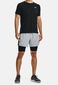 Svart atletisk t-shirt med korta ärmar, parat med ljusgrå shorts och svarta kompressionsshorts under. Inkluderar Under Armour-logotyp.