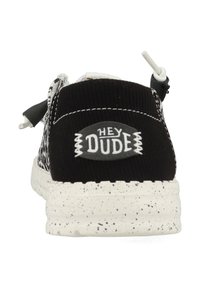 Scarpe slip-on in corduroy nero con suola bianca macchiata e logo "HEY DUDE" su una patch grigia sul retro. Scarpe dotate di lacci elasticizzati.