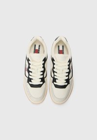 Beige and black sneakers with perforated design, lace-up closure, and rubber sole. Logo detail on side and interior branded tongue labels.