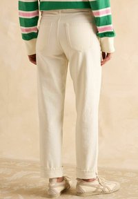 Kreemivärvi kõrge vöökohaga püksid sirge säärega, millel on kaks tagumist taskut ja üles keeratud sääred. Kanda heledate sneakerite kõrval.