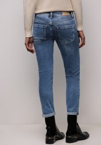 Jean en denim bleu clair à coupe slim, revers roulés, deux poches arrière et une étiquette en cuir beige à la ceinture.