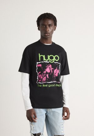 Black cotton t-shirt with lime green and pink graphic print, featuring a distressed round neckline and relaxed fit. Paired with distressed light blue jeans.