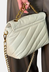 Borsa a tracolla in pelle crema trapuntata con manico e cinghia in oro. Presenta una texture liscia e doppi accenti in catena sulle spalle.