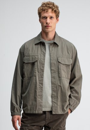 Light olive green shirt jacket with a relaxed fit, snap closures, two chest pockets, and elastic cuffs, made from soft fabric.