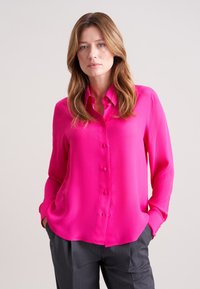Lys pink skjorte med knaplukning lavet af glat stof, med krave, lange ærmer og en afslappet pasform, parret med grå snepskurede bukser.