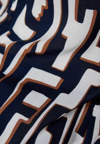 Marineblauer Stoff mit großen weißen und braunen geometrischen Mustern, mit einer glatten, leicht strukturierten Oberfläche.