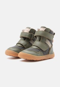 Grüne Lederstiefel mit mandelförmiger Zehenkappe, zwei Klettverschlüssen, grauen Akzenten, weicher Innenausstattung und einer braunen Gummisohle. Entwickelt für Komfort und Unterstützung.