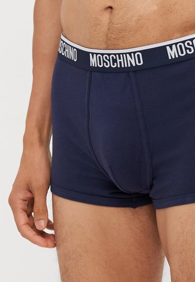 Prazni bokserice tamnoplave boje od mekog pamučnog materijala, s bijelim elastičnim pojasom na kojem se u podebljanim slovima nalazi logo "MOSCHINO".