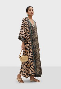 Kaftan en imprimé léopard avec accent turquoise, design fluide et manches larges. Associé à un sac à main doré et des sandales plates.