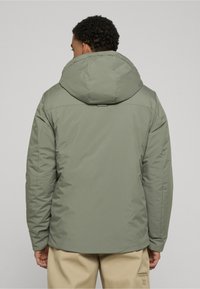 Green padded jacket with a large hood, featuring a smooth texture and a rounded design. Back view shows a simple cut and stitching details.