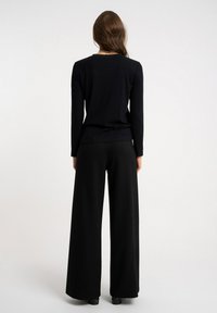 Czarna bluzka z długim rękawem o dopasowanym kroju i okrągłym dekolcie, zestawiona z czarnymi spodniami o szerokich nogawkach. Gładka, miękka faktura, bez widocznych wzorów.