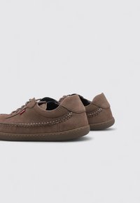 Zapatos de cuero marrón con un acabado texturizado, que presentan un detalle cosido alrededor de la suela, cordones y un pequeño acento rojo en el costado.
