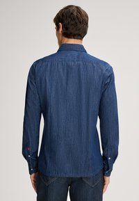 Camicia in denim blu scuro con maniche lunghe, polsini con bottone e colletto. Presenta un taglio dritto e una sottile texture con dettagli al yoke posteriore.