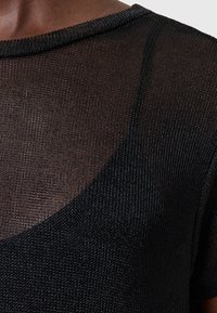 Gennemsigtig sort striktop med rund halsudskæring og korte ærmer. Teksturert stof med et subtilt, åbent vævemønster.