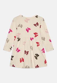 Långärmad klänning i ljus grädde med resår i midjan, prydd med ett mönster av färgglada rosetter i rosa, röd, mörkröd och brun. Tillverkad av bomull.