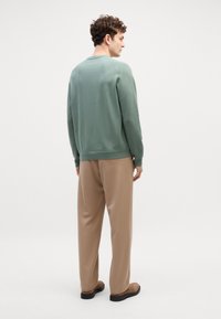 Maglione verde a coste con collo tondo, abbinato a pantaloni beige. L'outfit presenta una vestibilità rilassata e un design minimal.