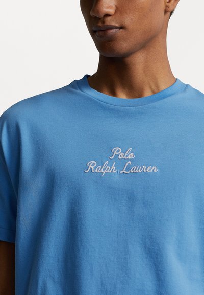 Tricou din bumbac albastru deschis cu guler rotund. Prezintă text alb brodat: "Polo Ralph Lauren" centrat pe piept.